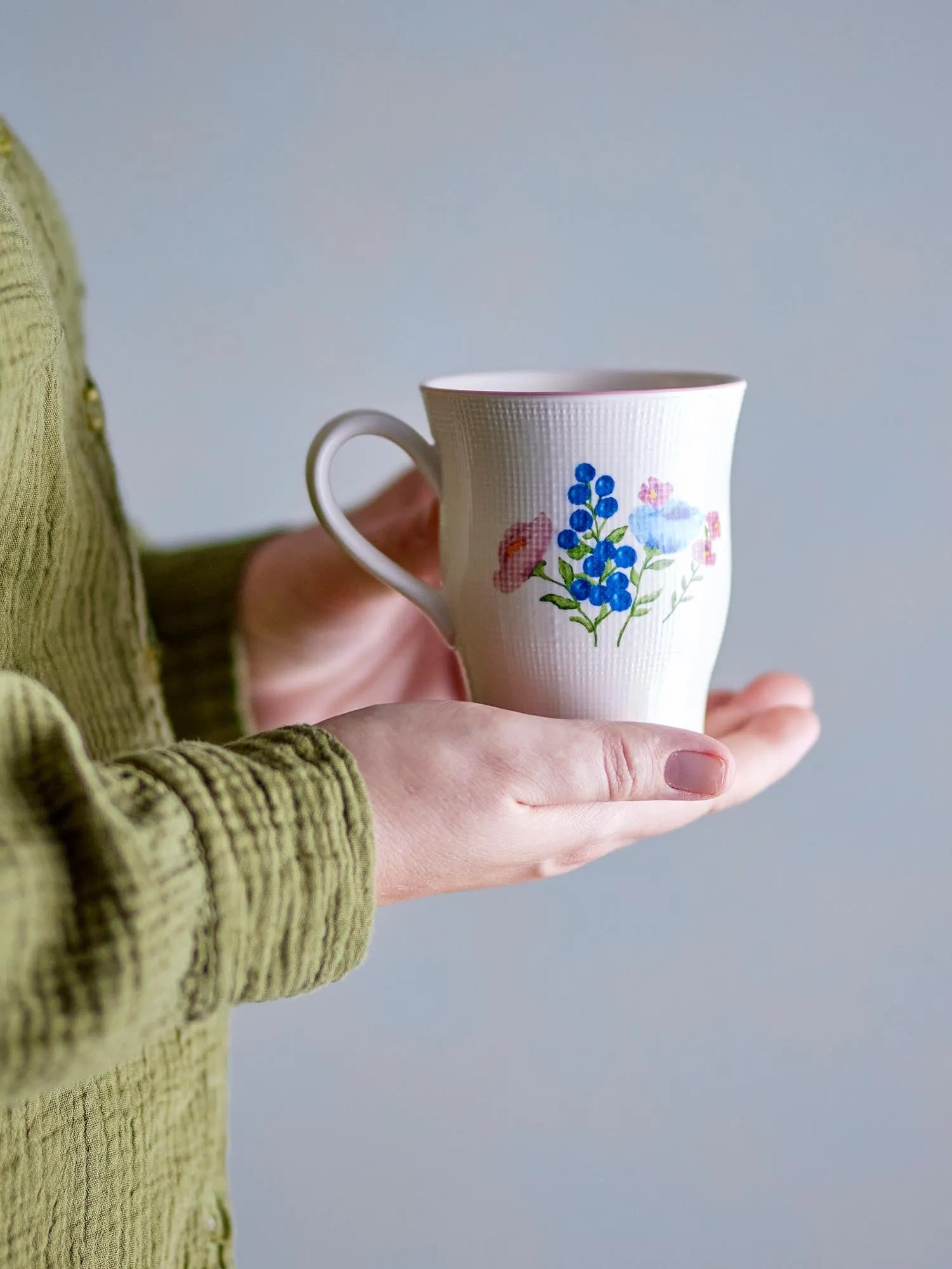 Ein stilvoller Steingutbecher mit geprägtem Blumenmotiv in lebendigen Farben und rosa Rand, ideal für Kaffee oder Tee.